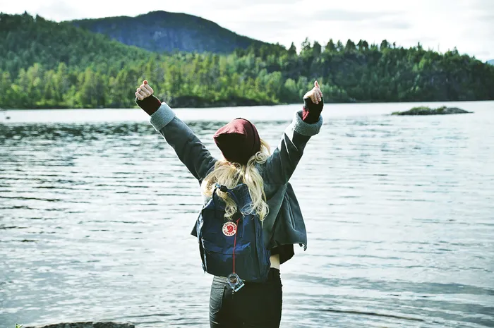 A woman standing infront of a lake, looking at the horizon, with raised hands