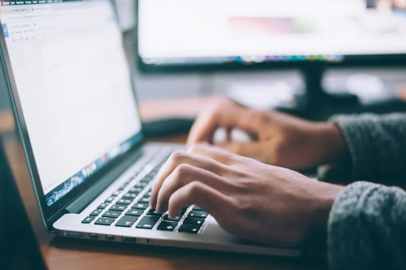 A white screen laptop and two hands typing on the laptop